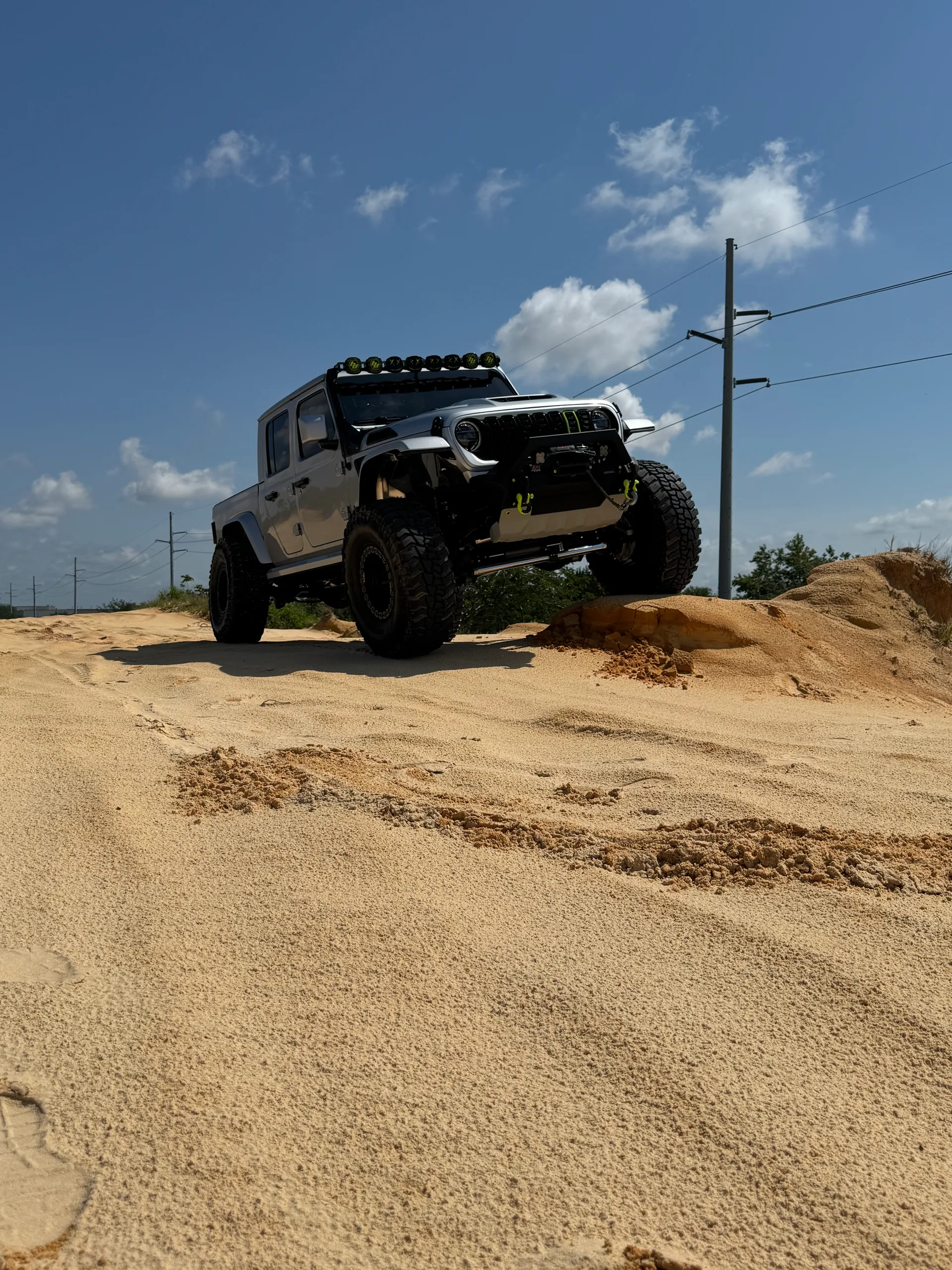 Gray Jeep Gladiator off-road on sandy dunes under blue Florida sky